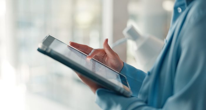 Close-up of a business professional in a blue shirt tapping a tablet screen in a bright office setting