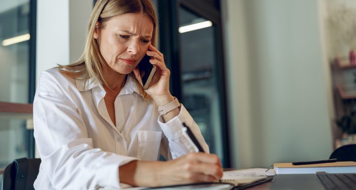 Concerned businesswoman on the phone taking notes at her desk, reflecting the stress of receiving a CIPA demand letter
