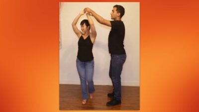 Pareja bailando bachata, realizando un giro con dos manos.