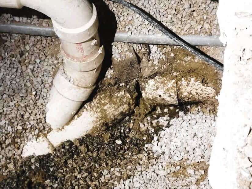 A close-up image of a leaking, damaged water pipe buried under gravel.