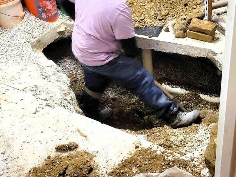 Construction workers dig out space under concrete flooring to replace broken and leaking water pipes and part of slab leak repair.
