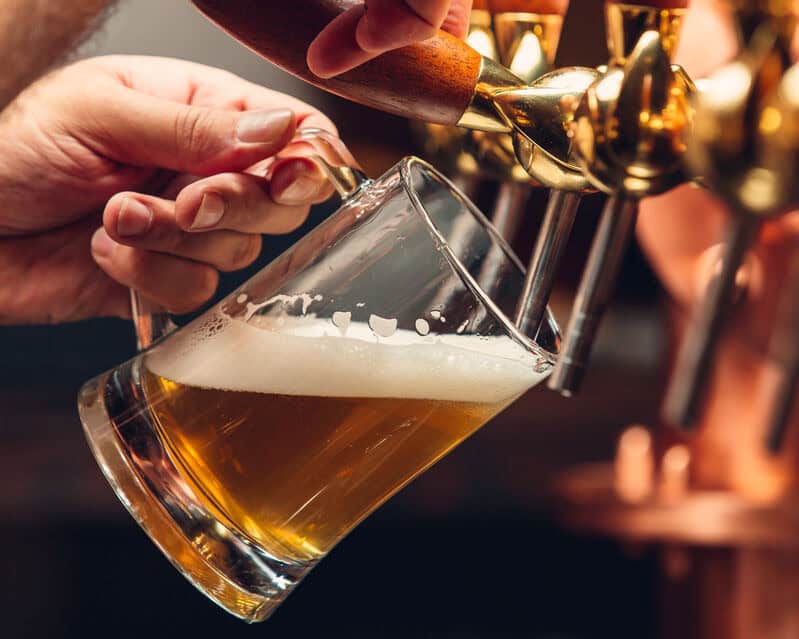 A tilted glass mug is being filled with a delicious amber beer direct from a tap in a taproom.