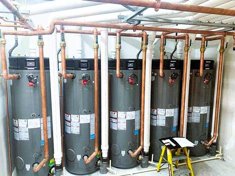 A row of five water heaters all connected to copper pipes. This redundant water heater setup ensures there's always a backup water heater in case of a hot water emergency.