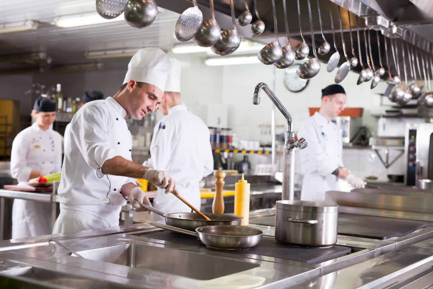 Chefs work in a hotel restaurant kitchen surrounded by pots and pans.