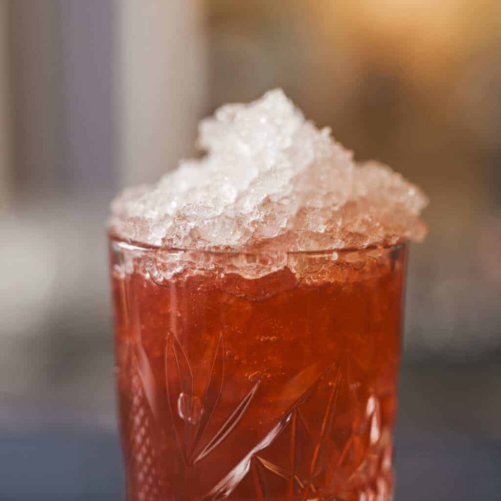 A red cocktail in a clear glass full of crushed ice.