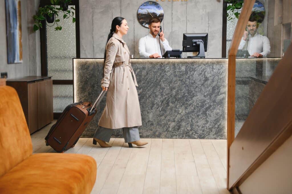 Female guest in a trenchcoat and  come with bags and suitcases to the hotel reception in the lobby.