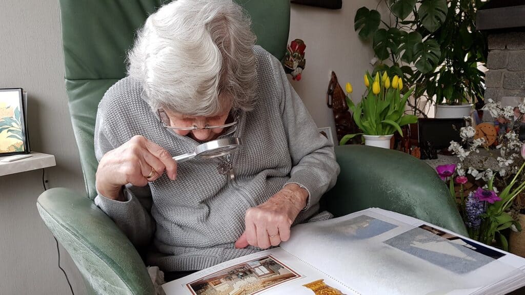 An older woman uses a magnifying glass to look at a photo album. Moving to a senior care facility can take some adjustment, but it can be a good idea for aging parents.