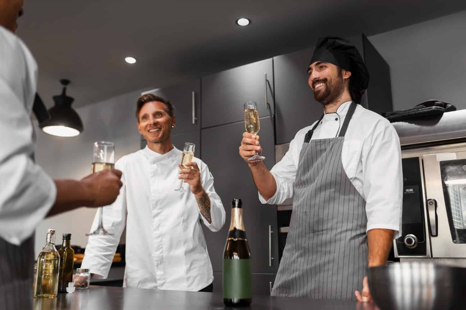 A team of three chefs stand around a table, holding champaign flutes, cheering a successful night in their restaurant.
