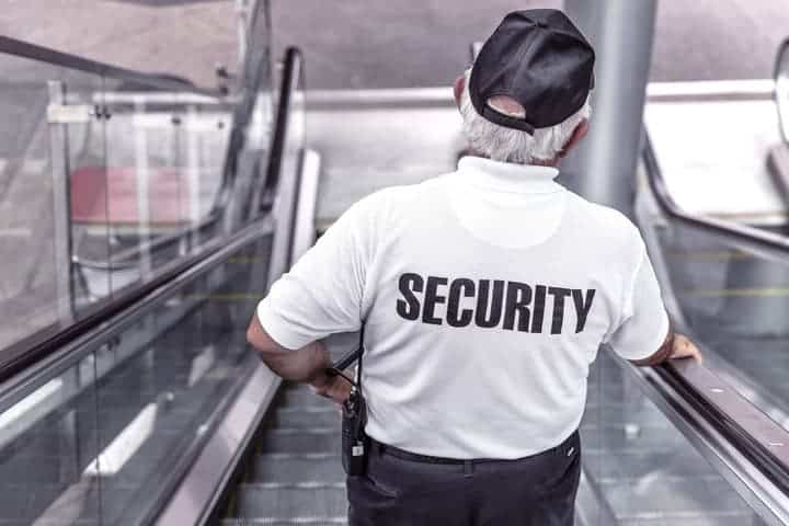 A man with the word "Security" on the back of his uniform goes down an escalator. Hotel security guards can help give guests peace of mind when staying at your hotel.