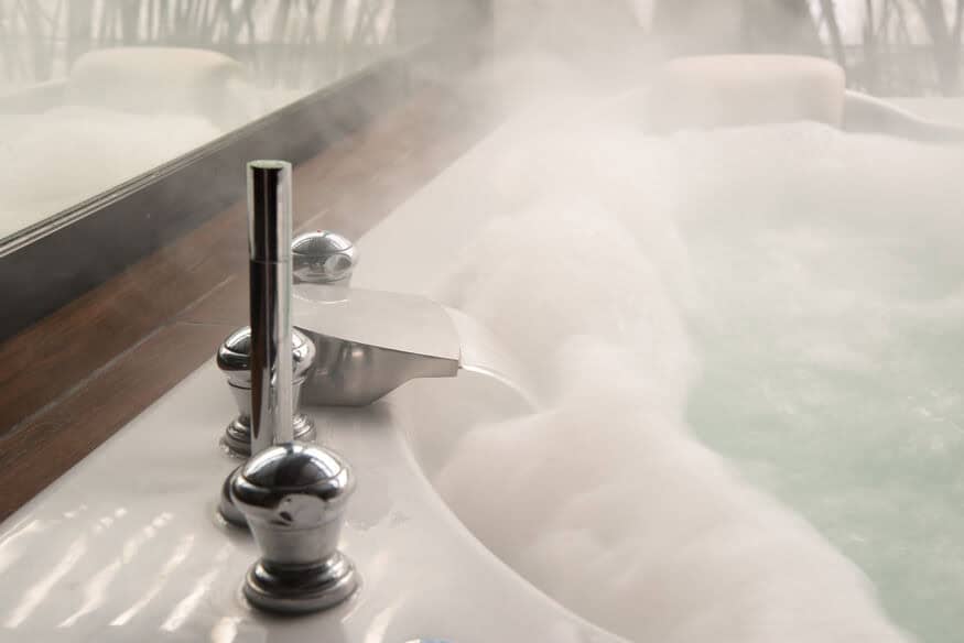 Steamy hot water pours from a faucet into a spa-like bathtub with a large mirror on its left side. Commercial boiler heating systems can keep your customers satisfied. 