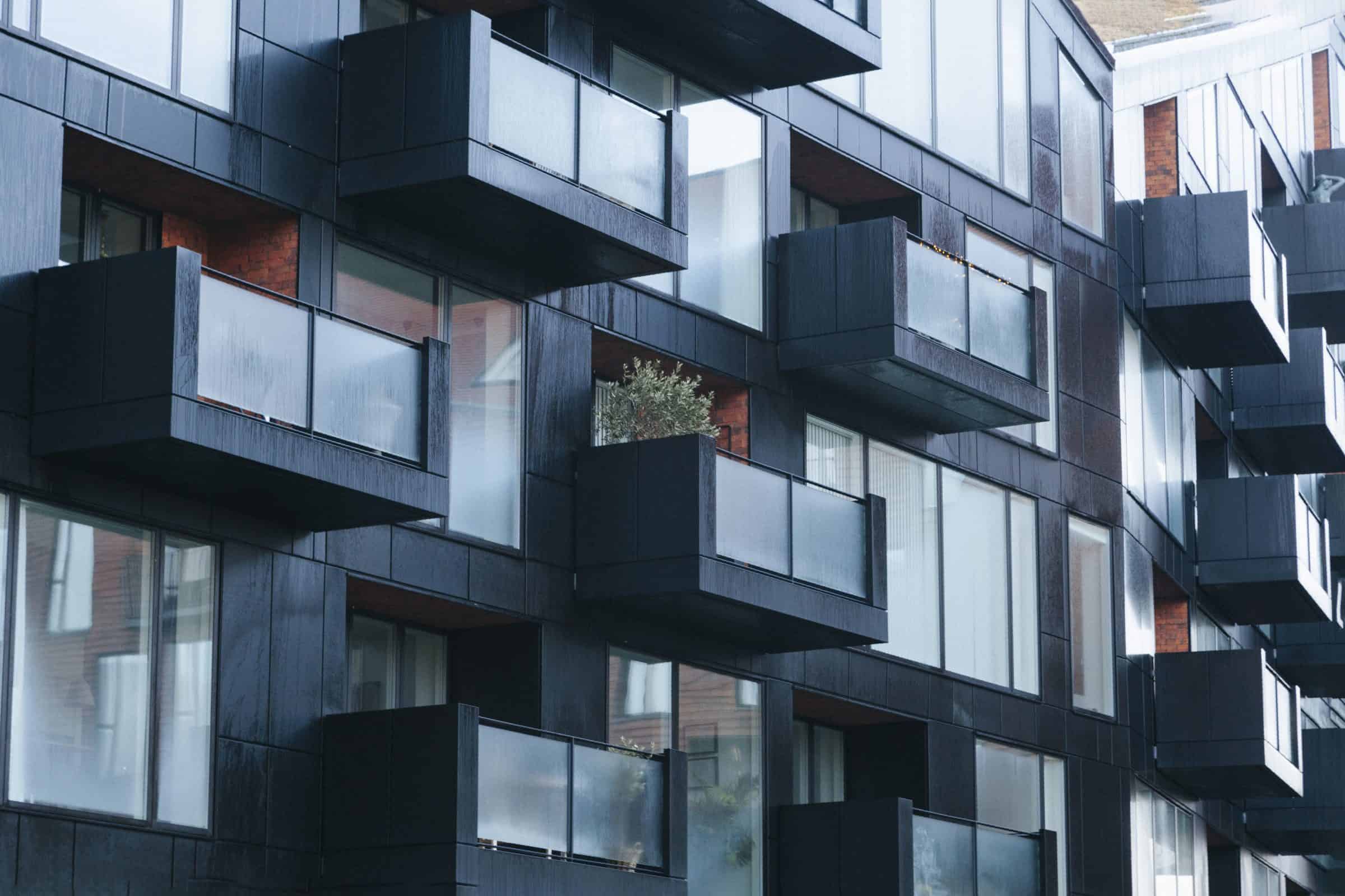 The outside of an apartment complex is black with squares of balconies jutting forward.