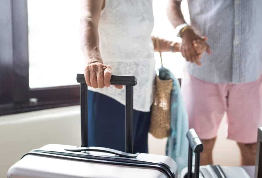 A couple is holding hands and standing near suitcases as they check into a hotel for their vacation.