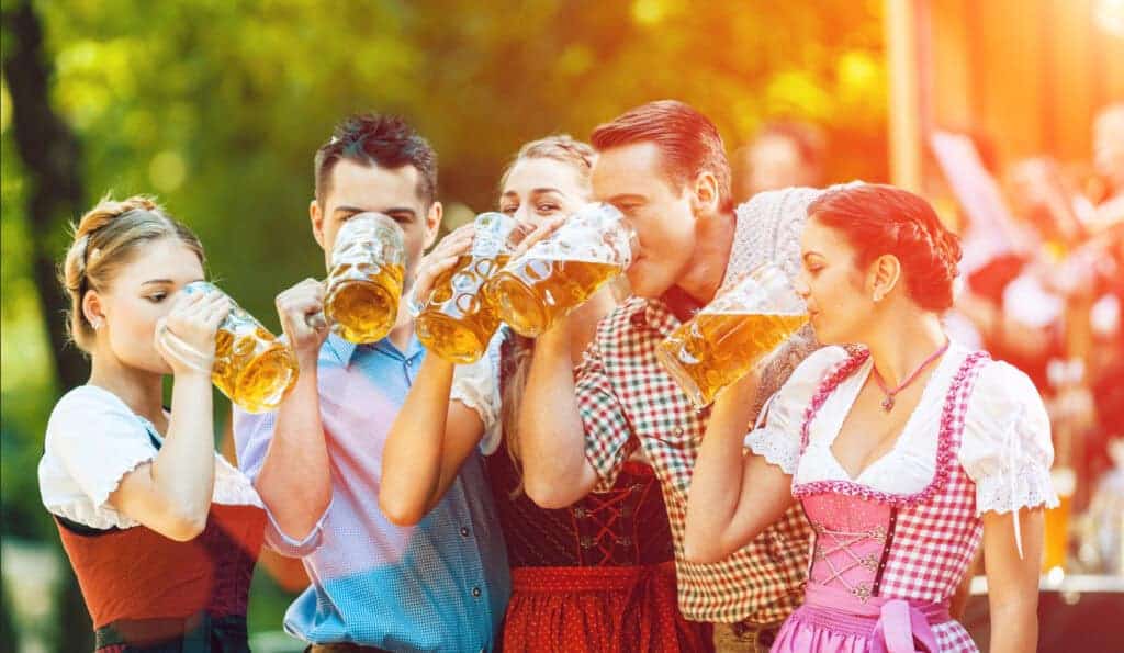 Men and women dressed for Octoberfest drink beer from large glass steins in a friendly outdoor beer garden.