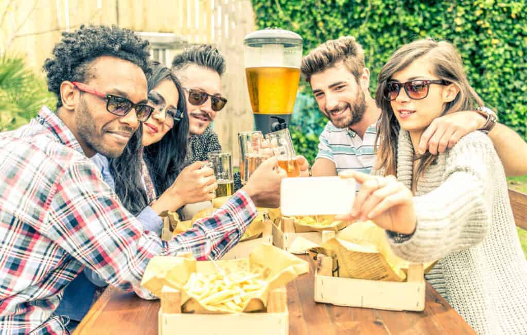 Friends enjoy beer and food while sitting at a picnic table in an outdoor beer garden.