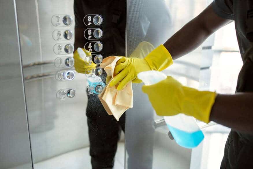 A man wearing yellow rubber gloves sanitizes the buttons of an elevator in the lobby. 
