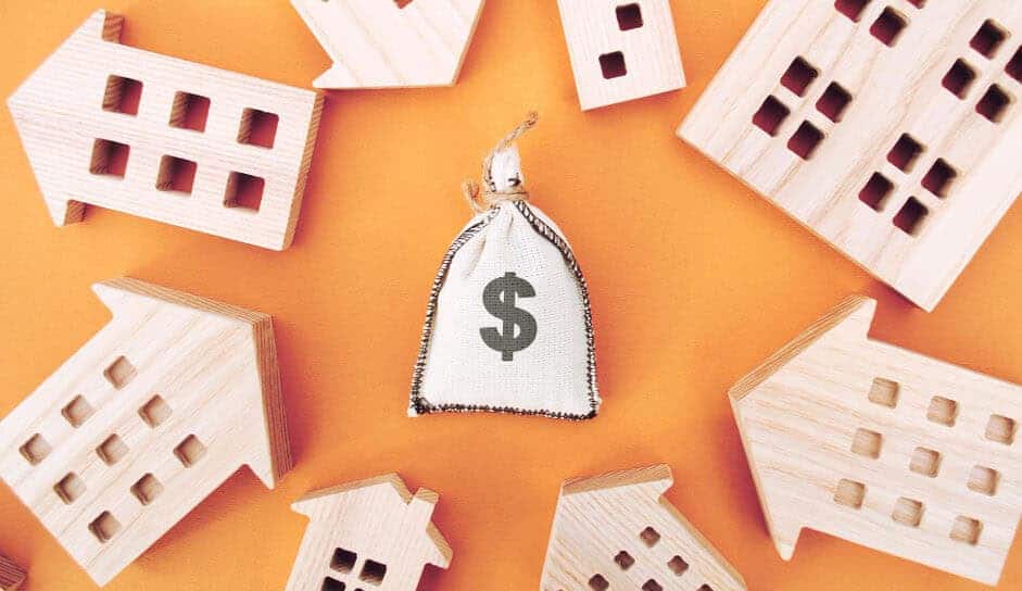 Wooden apartment cutouts surround a canvas bag with a dollar sign on it. Landlords rely on timely rent payments. 