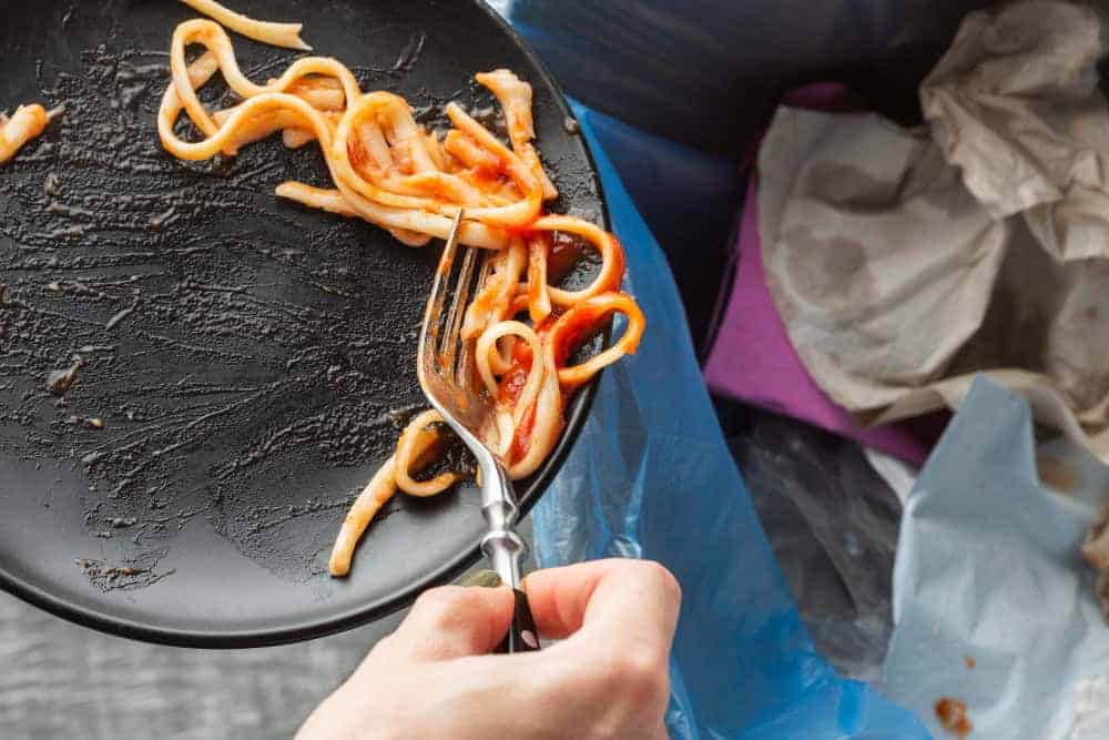 Leftover spaghetti is being scraped into a bin. This is called "post-consumption food waste."