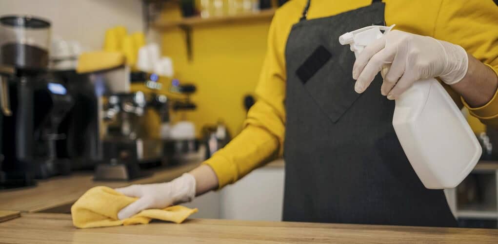 Side view of employee spraying and wiping down the counter of a coffee shop.