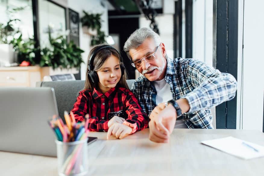 A grandfather with a short white beard uses a cell phone with his young granddaughter.