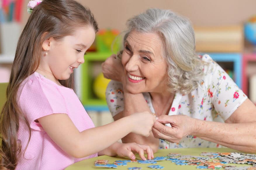 A young girl and a smiling senior citizen gather puzzle pieces.