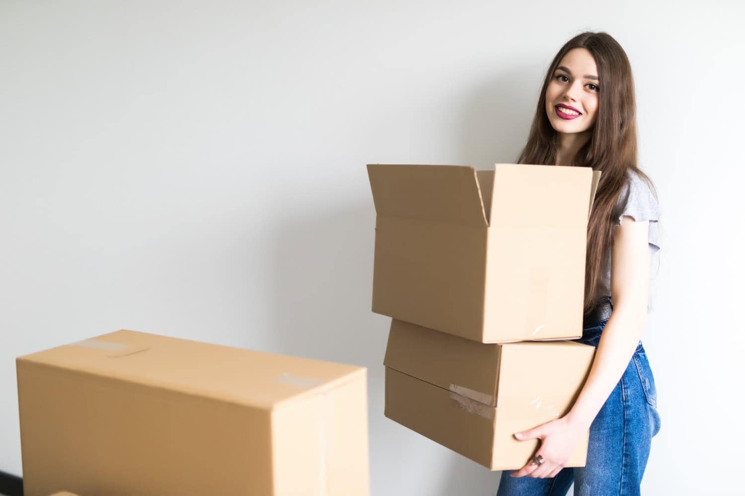 A young woman carries cardboard boxes as she moves out of an apartment. Here's how to tell if there's any property damage or normal wear and tear in her unit.