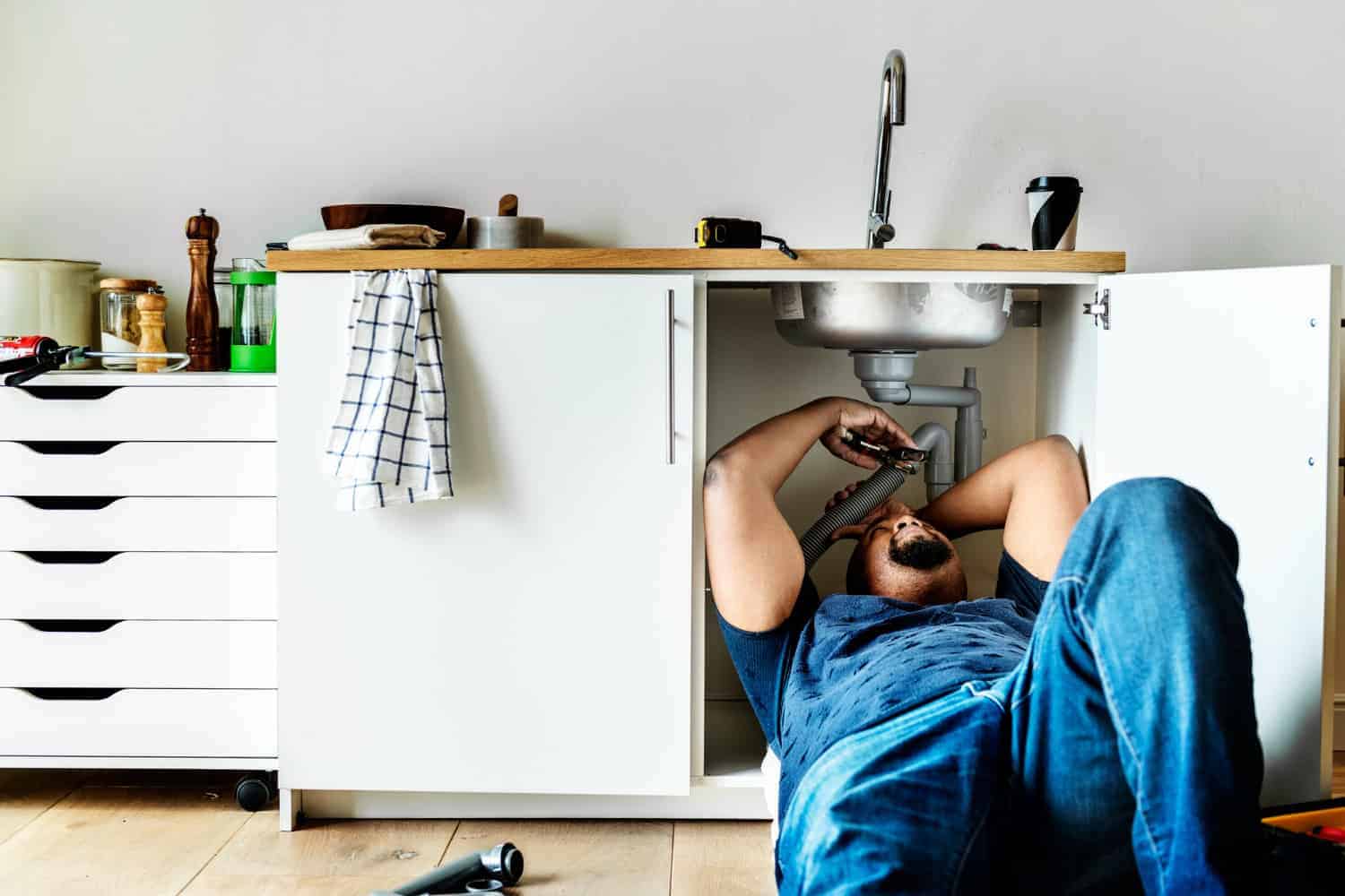 A handyman repairs the pipes under a leaking sink.