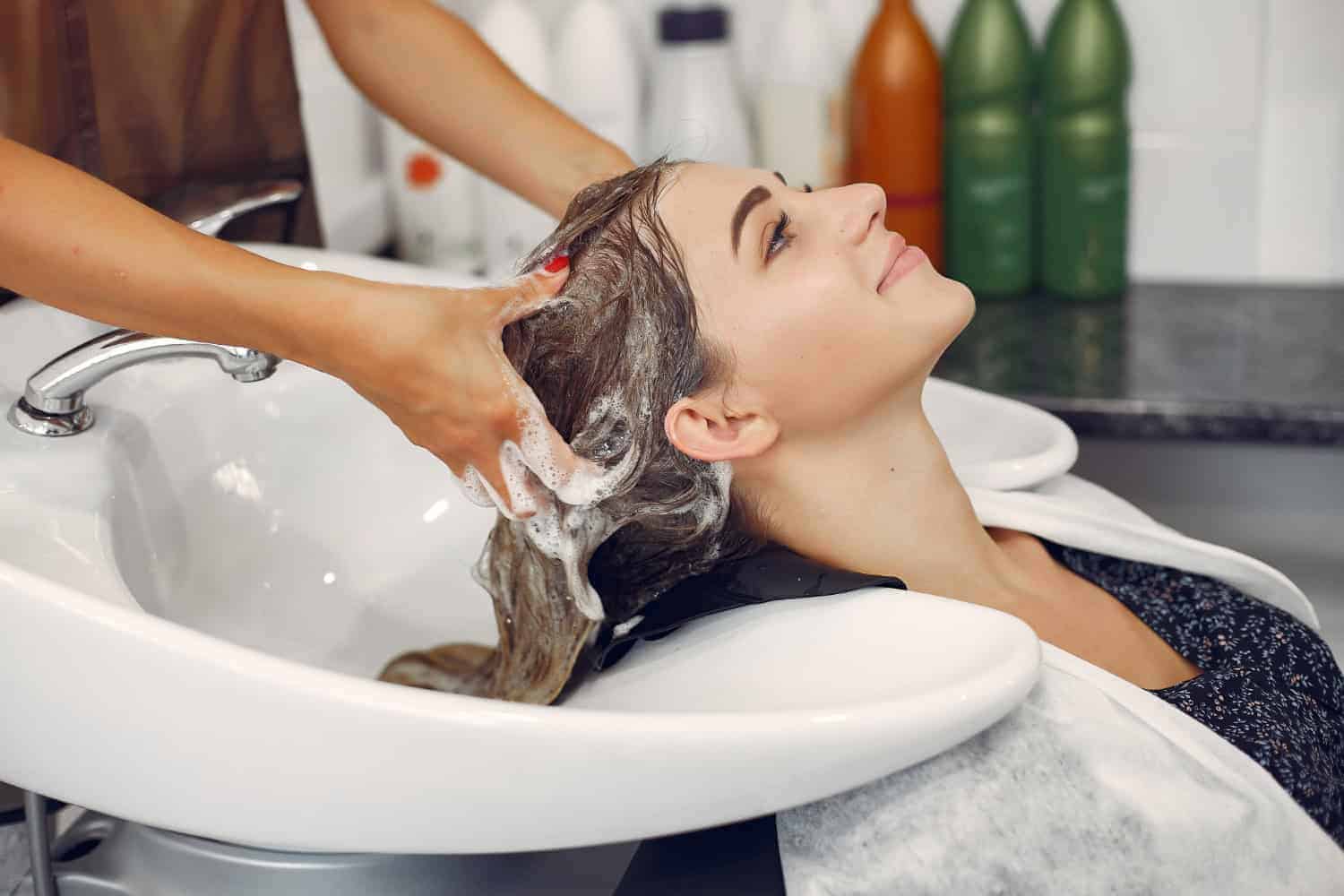 A woman at a salon hair washing station having her hair washed with shampoo and hot water.