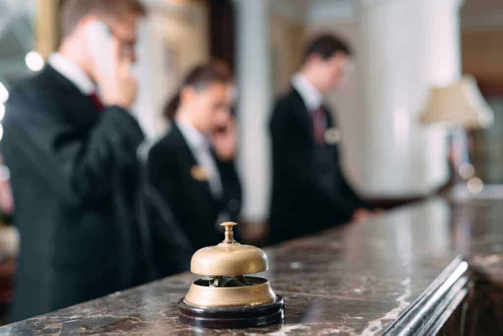 A hotel concierge bell on a desk, with hotel concierge staff in the background.