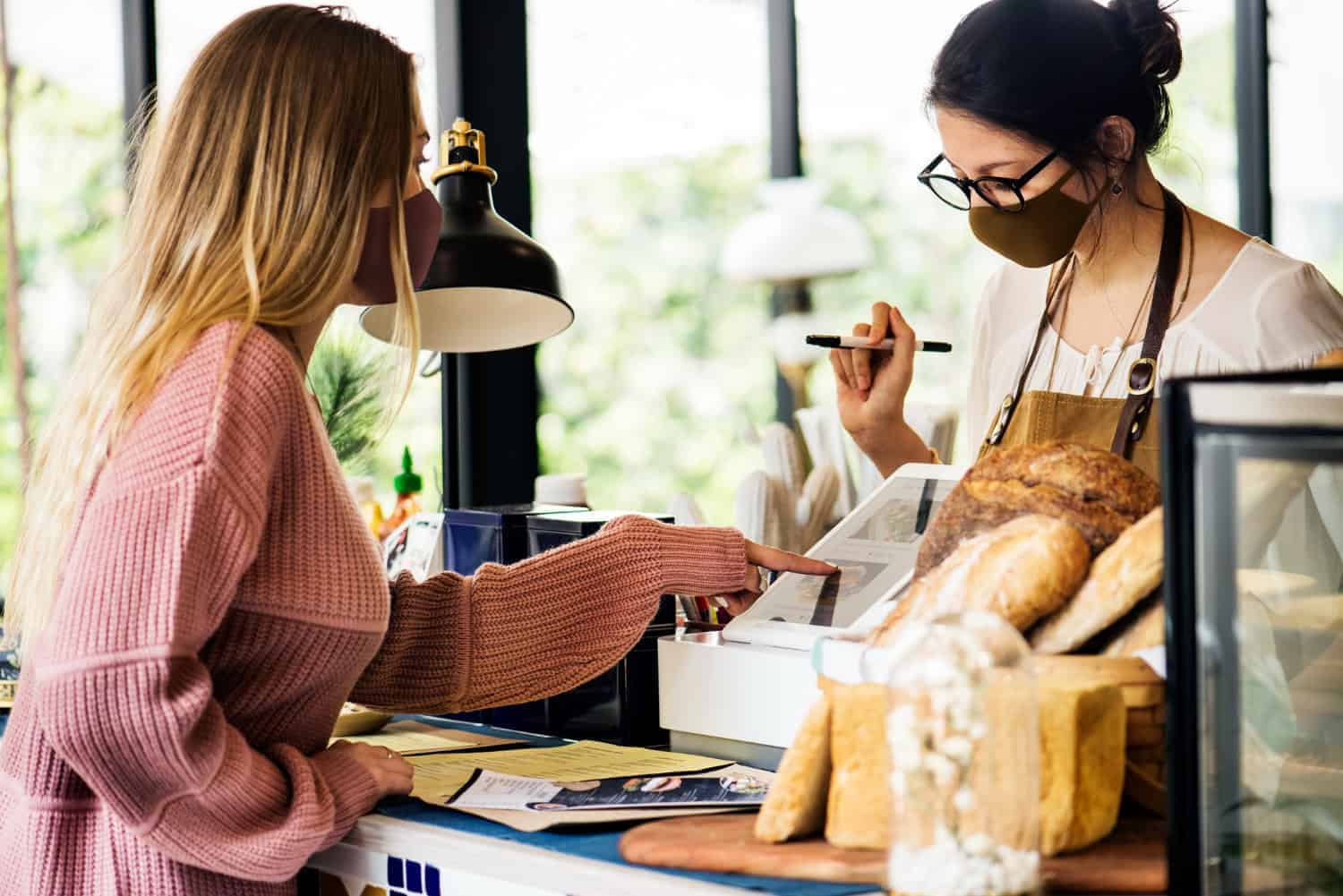 A restaurant customer placing and order at the counter, using a touch screen to complete her purchase while the cashier rings her up.