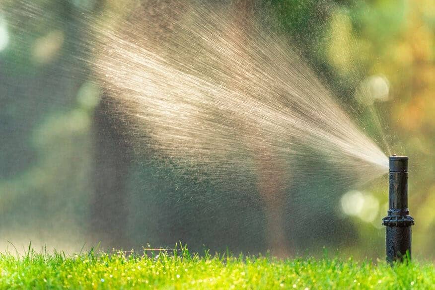 A close-up of a lawn sprinkler watering grass. You can learn how to reduce hot water usage in hotels by including landscaping water costs. 