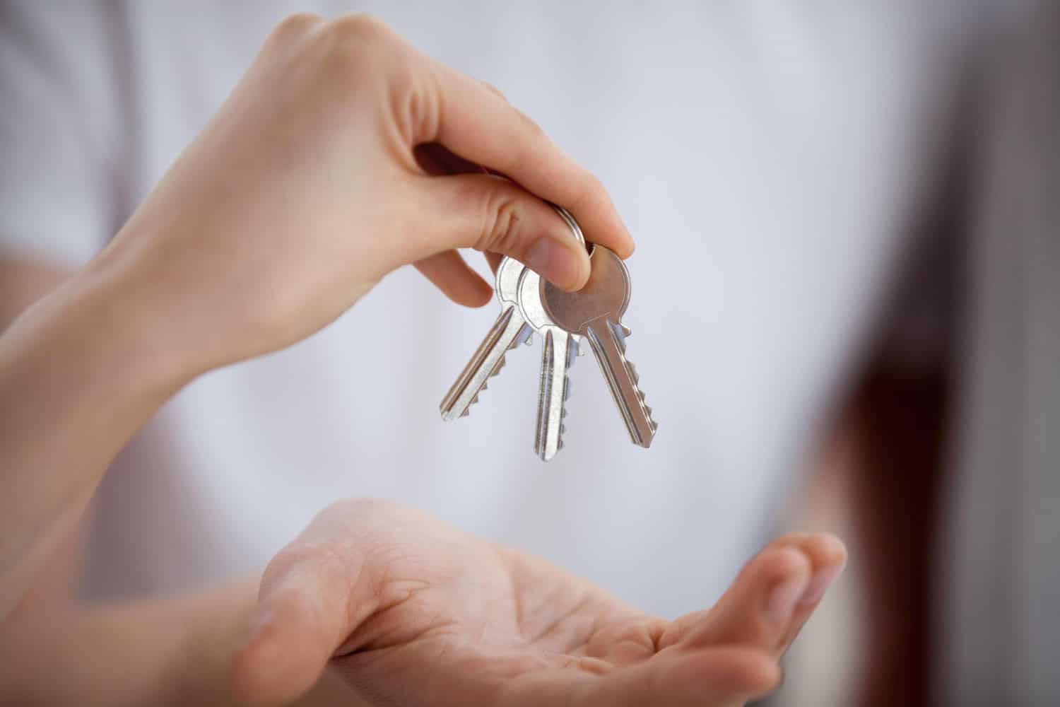 A landlord hands a tenant a set of three silver apartment keys.