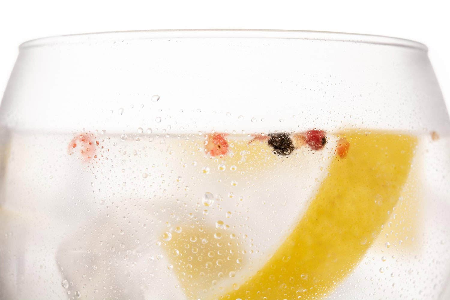 A clear glass filled with carbonated hard seltzer and garnished with a lemon wedge and berries.