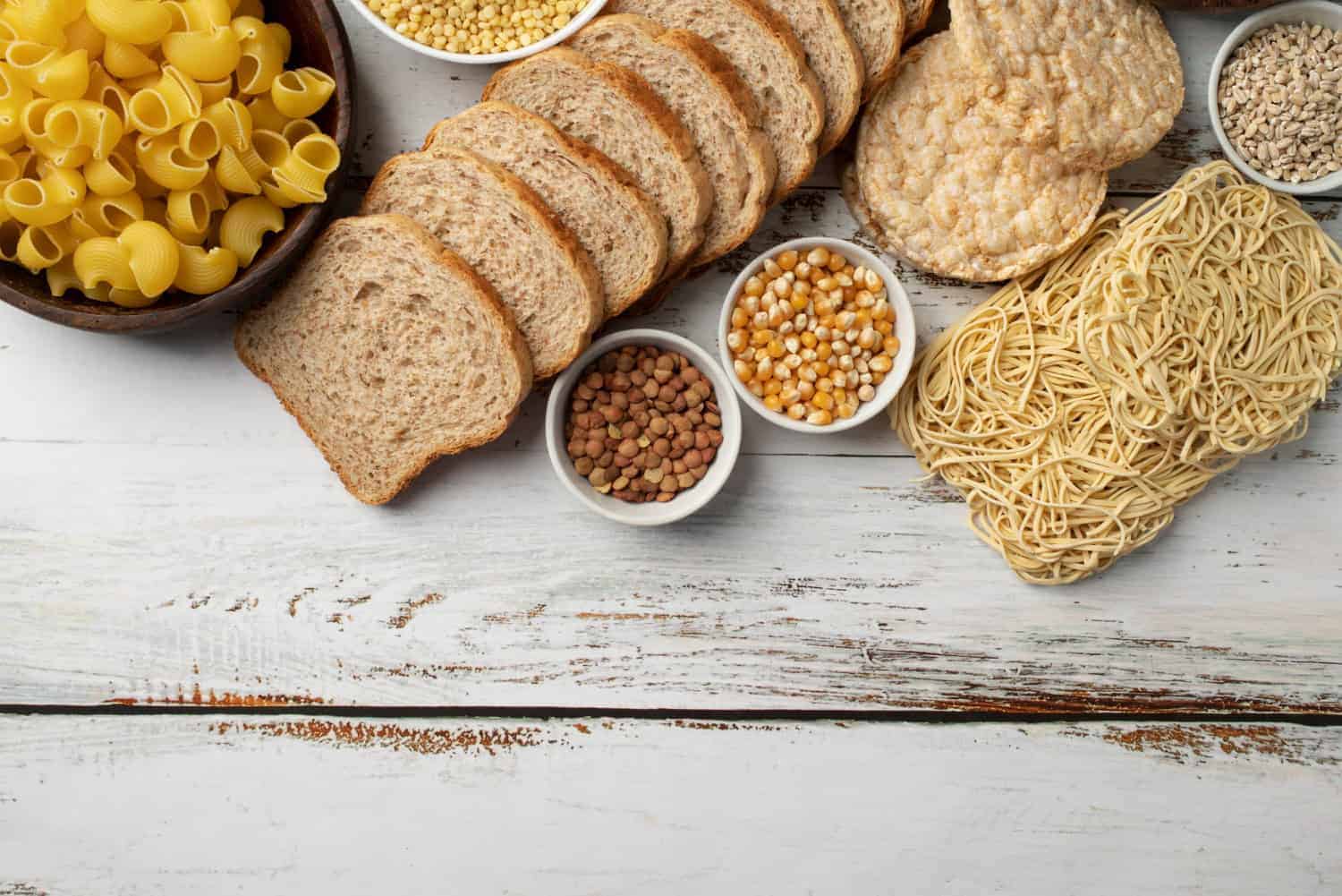 A collection of wheat-based foods - pasta noodles, bread, rice cakes, and grains - are all different kinds of food that contain gluten.