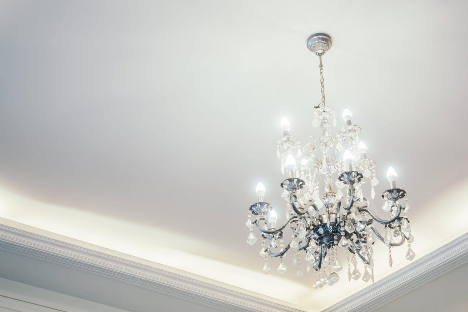 A large crystal chandelier hangs from a white ceiling, slowing bright white light.