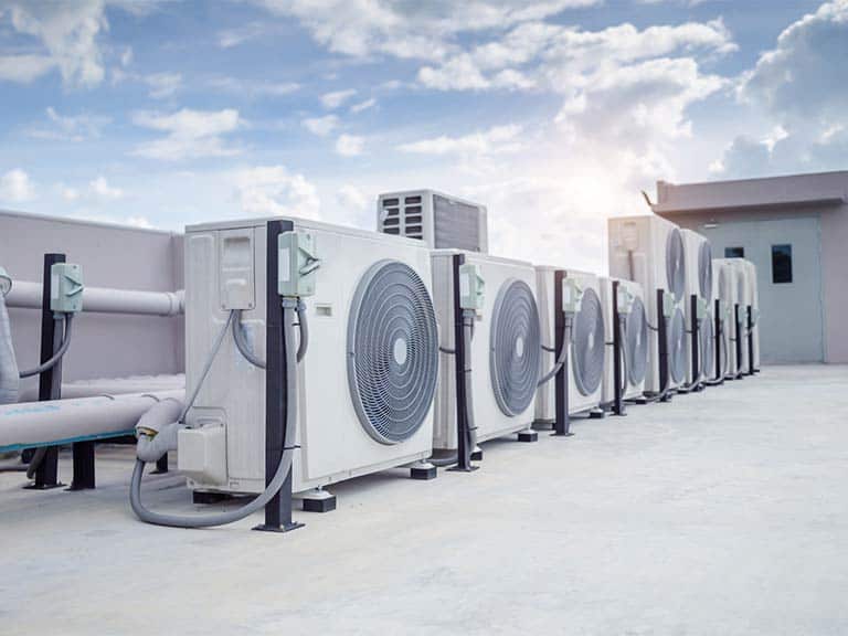 Several large fans as part of a rooftop HVAC system are shown with a blue sky and white clouds in the background.