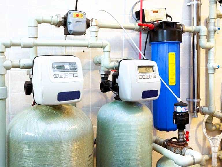 Two large water softeners are shown against a wall in a utility room.