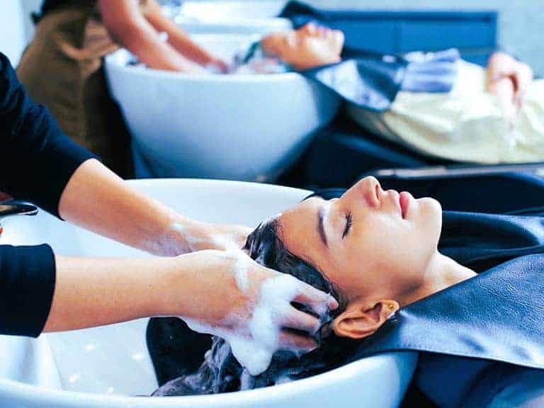 A woman sits at a basin in a salon getting her hair washed by another person.