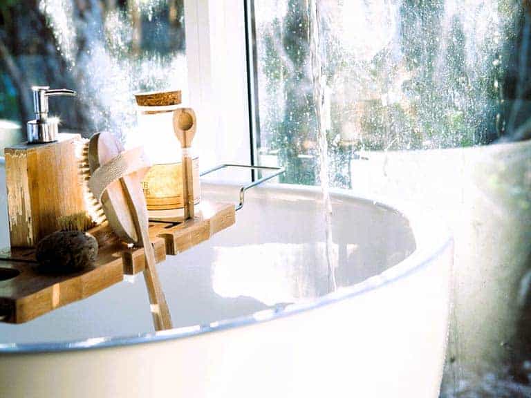 A white spa sink is shown near a mirror with lotions, oils and soap on a small wood shelf.