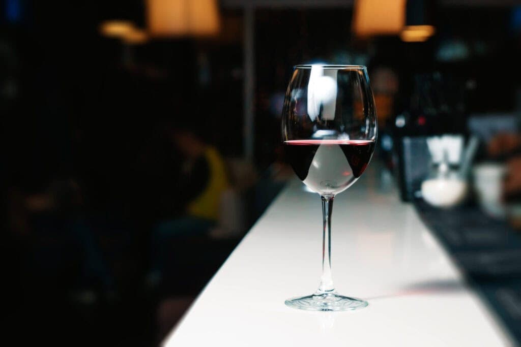 A glass of red wine sits on a long white bar countertop. Wine on tap can save bars money.