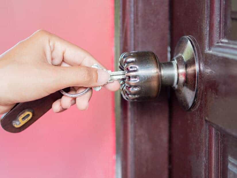 A woman's hand turns a key in a wooden door's lock.