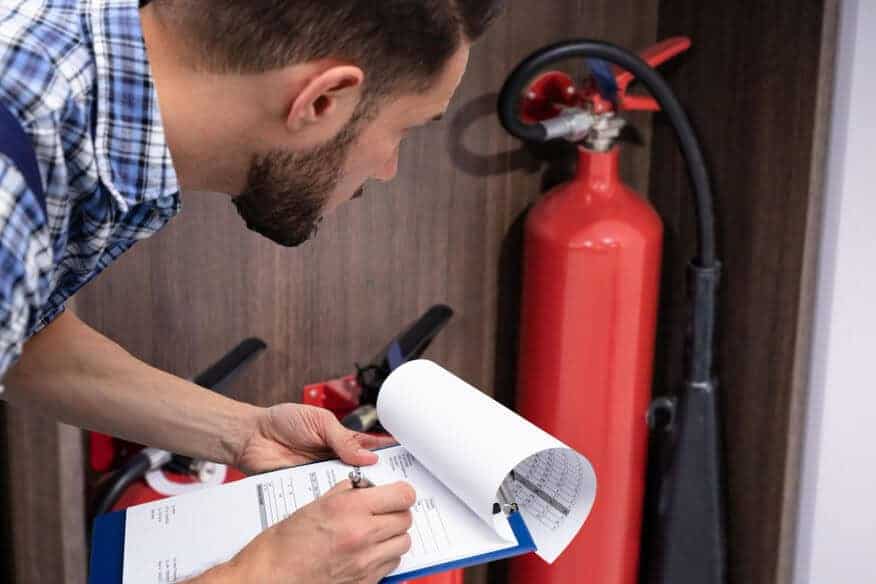 A man bends down to examine fire extinguishers and complete fire sprinkler maintenance.