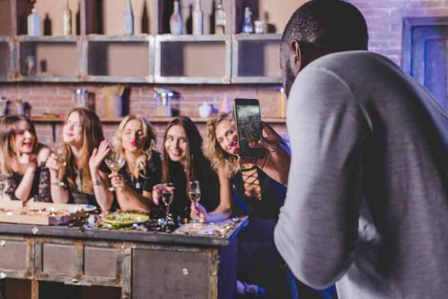 A man takes a picture of a group of women having fun at a restaurant for their social media feed.