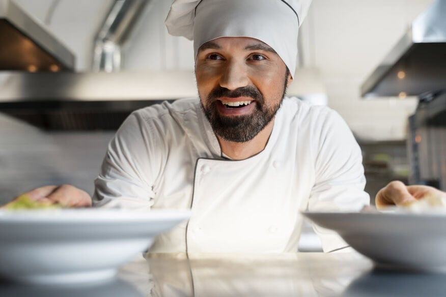 A smiling chef in uniform places two bowls of food made with the benefits of soft water on the commercial kitchen pass.
