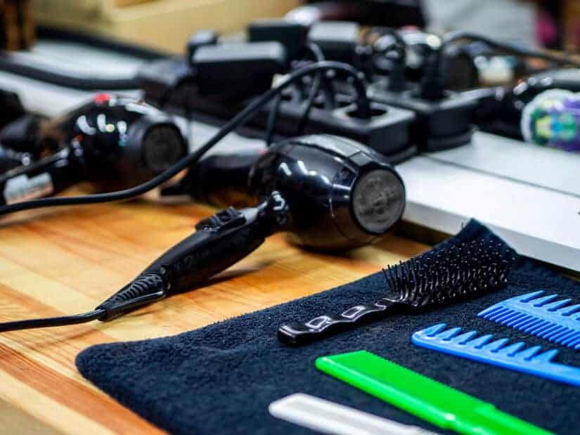 Hair dryers and combs on a salon shelf in front of a mirror. Stylist tools are just part of the salon maintenance checklist.