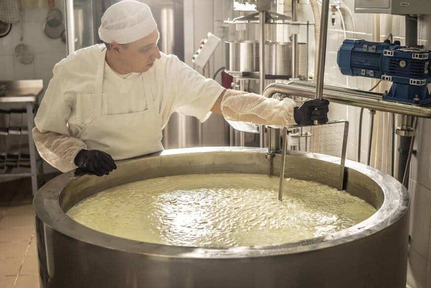 A man in protective gear aides a giant industrial mixer in stirring batter.