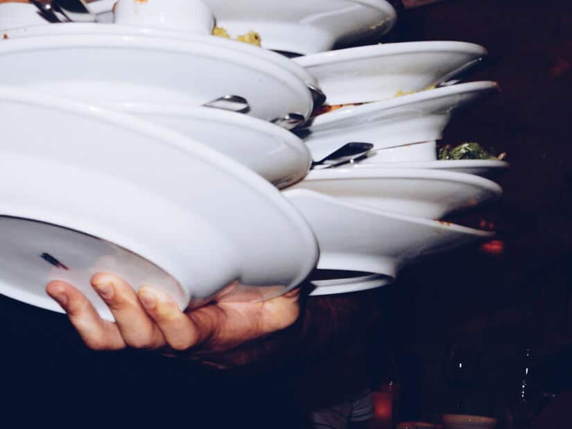 An impressive stack of dirty plates and utensils are stacked on an employee's hand, ready for dishwashing when restaurant water heaters fails don't happen. 