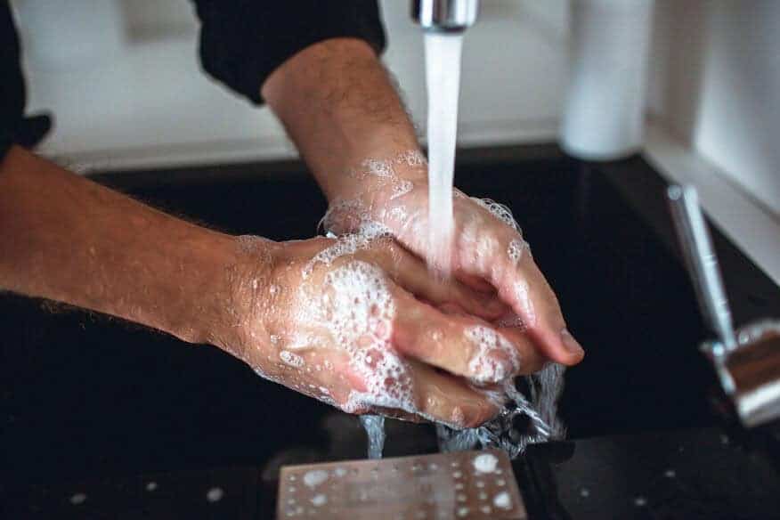A close-up of an employee washing his hands under hot water.