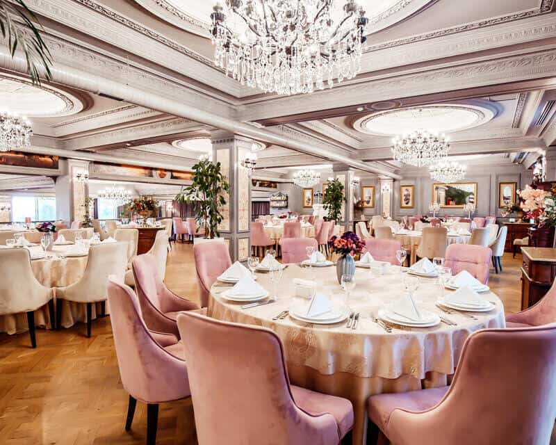 A pink and white-themed luxury hotel event space with round tables and chandeliers. Hotel event spaces have their own hot water demand. 