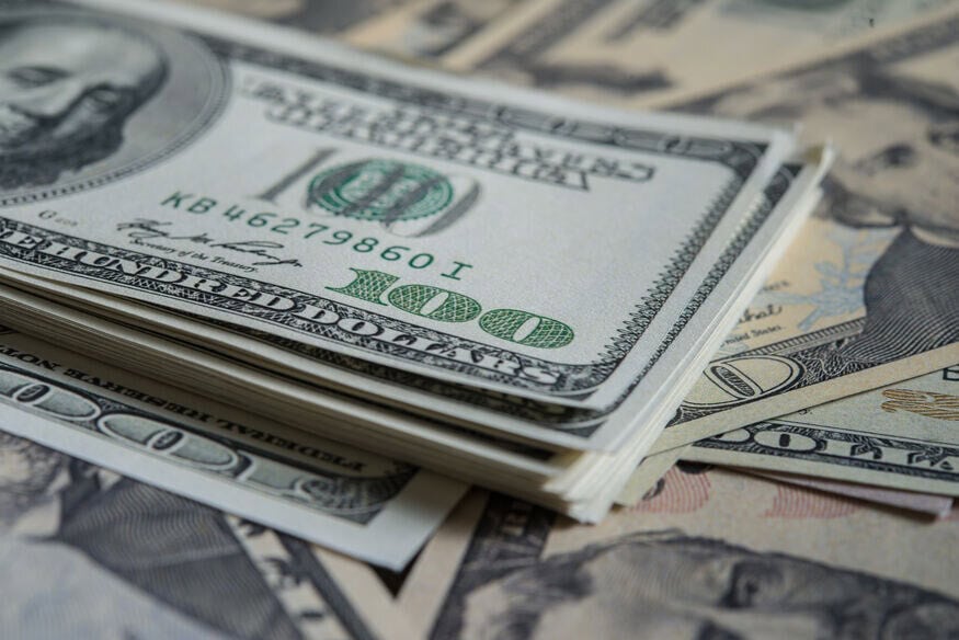 A stack of one-hundred-dollar bills on top of more bills lying across a surface, symbolizing the amount of money needed to buy, fix, and replace commercial water heaters when they no longer produce reliable hot water. 