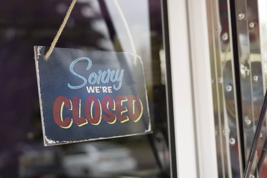 A “Sorry We’re Closed” sign hangs on the glass door of a business that is experiencing downtime after losing hot water from an old commercial water heater. 